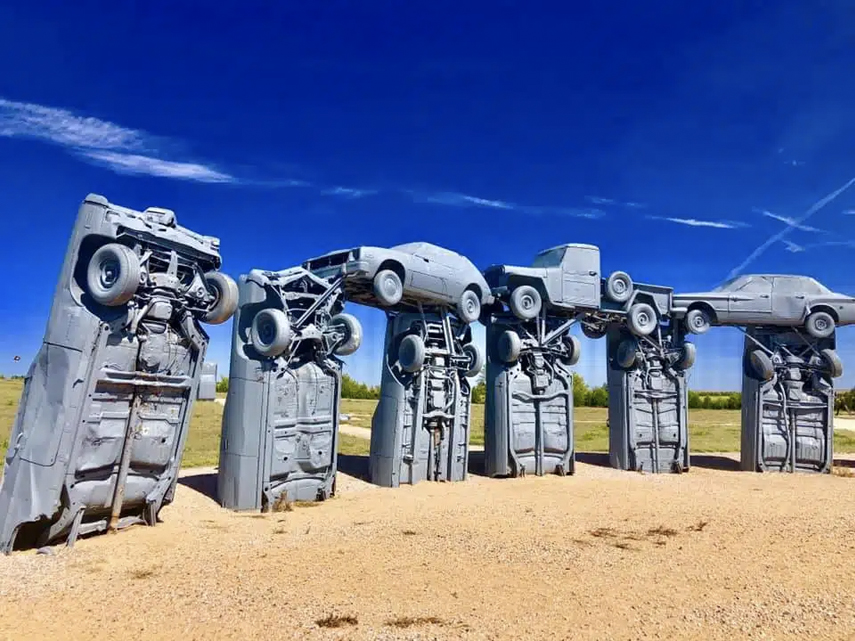 statues of painted cars stacking from the sand