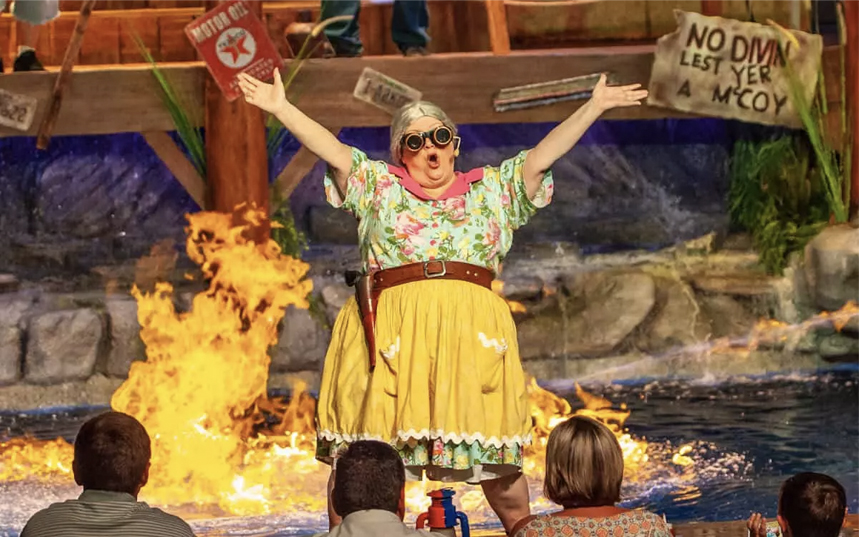 a female performer in goggles in front of the water and fire